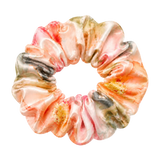 A mulberry silk scrunchie with a marbled watercolor floral pattern in peach, pink, beige, olive green, and dark gray, isolated on a transparent background.