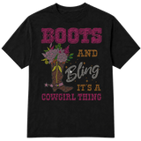 A black short-sleeve t-shirt with a western-themed rhinestone-style graphic that reads 'BOOTS AND Bling IT'S A COWGIRL THING' in pink, gold, and silver lettering, alongside an illustration of a cowboy boot decorated with flowers on a transparent background.