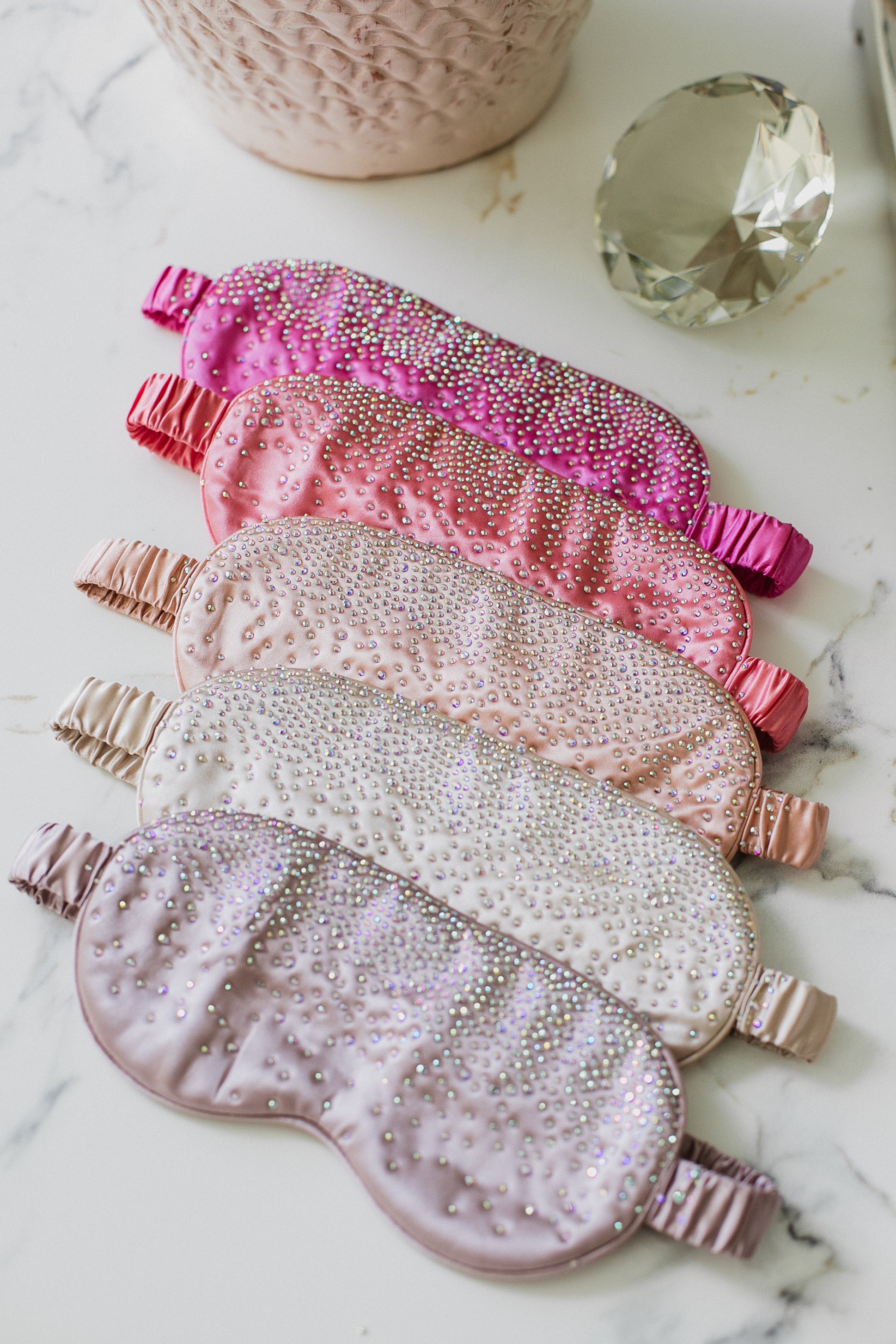 Set of rhinestone eye masks with rhinestone embellishments on a marble surface.