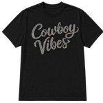 A black short-sleeve crewneck t-shirt featuring the words 'Cowboy Vibes' in a cursive script embellished with AB sparkling rhinestones that reflect multiple colors, shown on a transparent background.