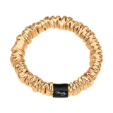 Gold skinny silk scrunchie with a black Brindy Label on a white background