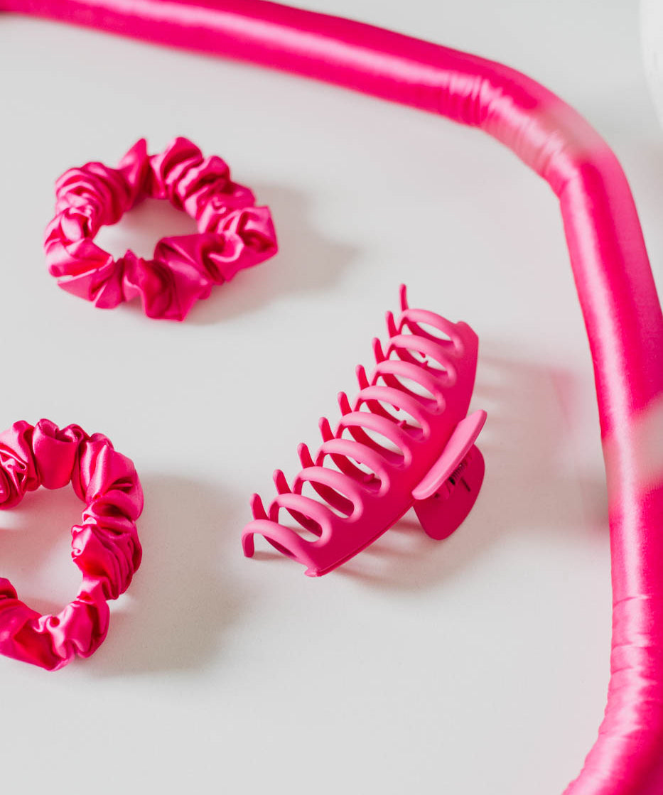 Hot Pink silk hair scrunchies and hair clip with a heatless hair roller rod on a white background