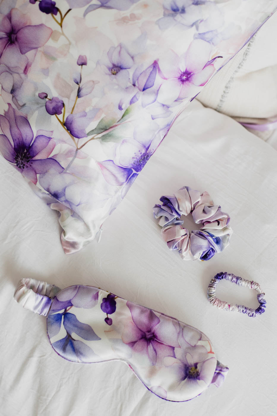 Set of purple floral-themed eye mask, hair tie, and sleep mask on a white background