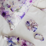 Set of purple floral-themed eye mask, hair tie, and sleep mask on a white background