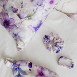 Set of purple floral-themed eye mask, hair tie, and sleep mask on a white background