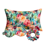 A floral-themed mulberry silk sleep set featuring a rectangular pillow, a matching eye mask, and a scrunchie, all decorated with a colorful watercolor-style rose pattern on a white background.