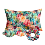 A floral-themed mulberry silk sleep set featuring a rectangular pillow, a matching eye mask, and a scrunchie, all decorated with a colorful watercolor-style rose pattern on a white background.