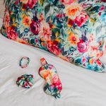 Floral mulberry silk pillowcase with matching scrunchie, eye mask, and bracelet on a bed.